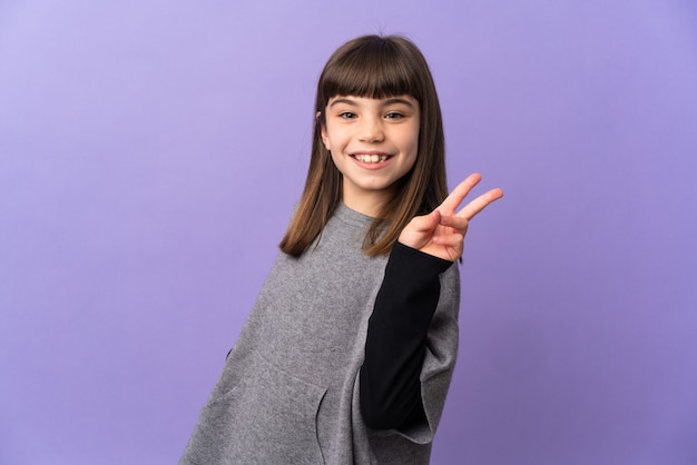 Little girl over isolated wall smiling and showing victory sign