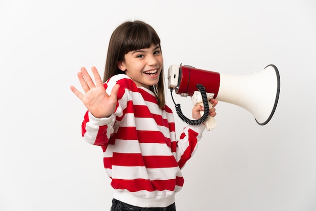 Little girl isolated on white background holding a megaphone and saluting with hand with happy expression