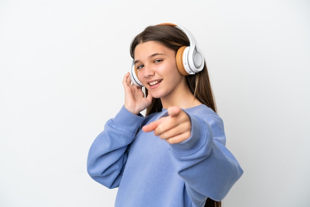 Little girl over isolated white background listening music and pointing to the front