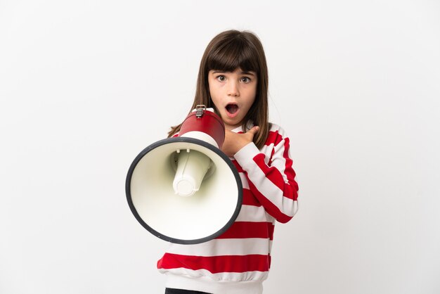 Little girl isolated on white background shouting through a megaphone with surprised expression