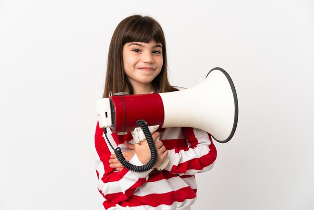 Bambina isolata sulla parete bianca che tiene un megafono e sorridente