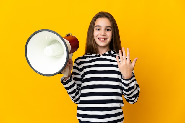 Little girl isolated on yellow background holding a megaphone and inviting to come with hand