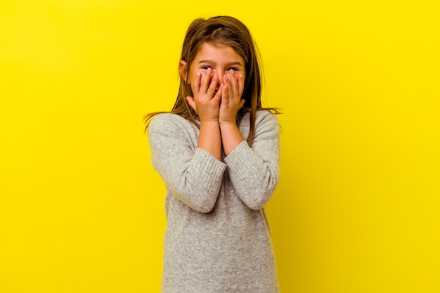 Little girl isolated on yellow wall laughing about something, covering mouth with hands