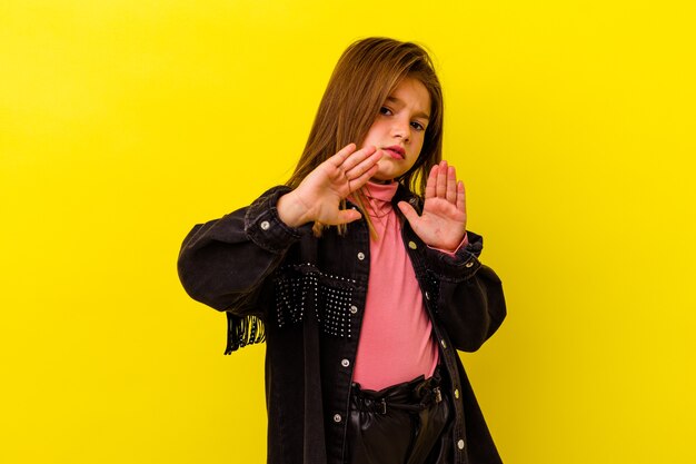 Little girl isolated on yellow wall rejecting someone showing a gesture of disgust
