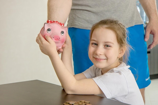 Little girl joyfully takes a piggy bank from her father's hands