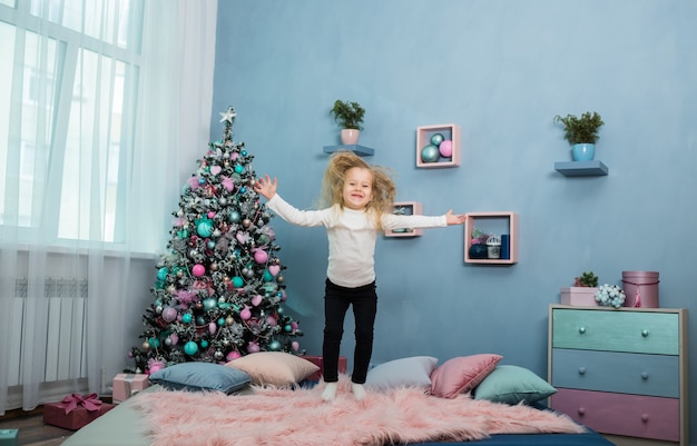 Little girl jumps on the bed against the Christmas tree