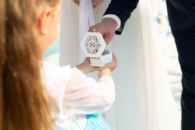 Una bambina tiene le fedi nuziali in una piccola scatola cerimonia di nozze all'aperto
