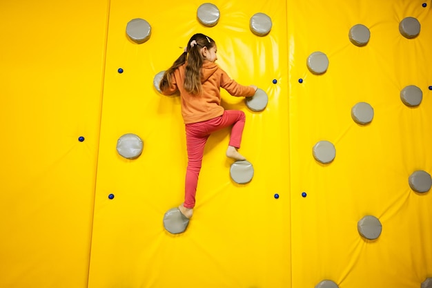 Стена для скалолазания маленькой девочки в парке желтой игровой площадки Ребенок в движении во время активных развлечений
