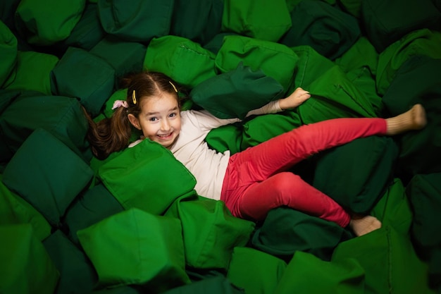 Little girl kid lies on green soft cubes at playground park Child in active entertaiments