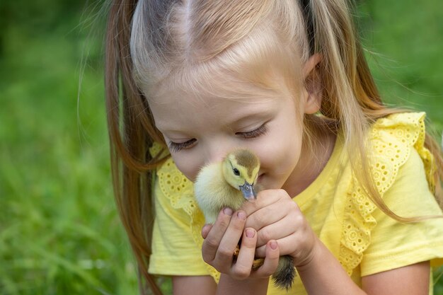 A little girl kisses a duckling which she holds in her hands on a summer day