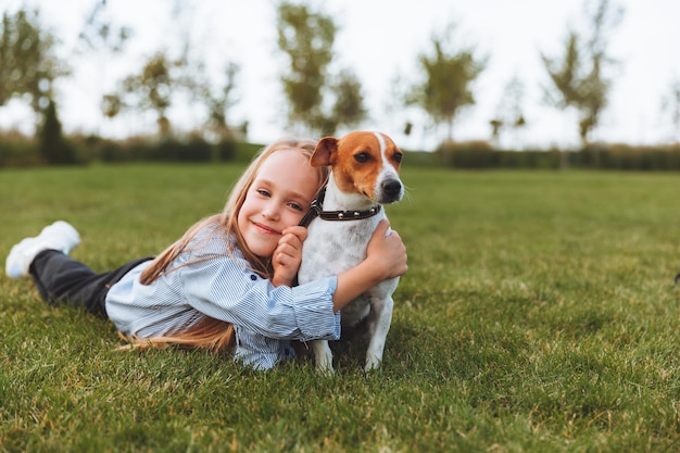 A little girl kisses and hugs her jack russell terrier dog in\
the park love between the owner and the dog a child is holding a\
dog in his arms