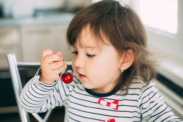 かわいいさくらんぼを食べる台所の少女