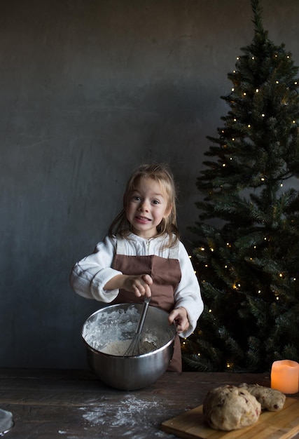 A little girl kneads dough at a Christmas table decorated with candles