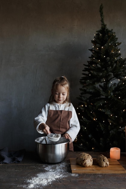 A little girl kneads dough at a Christmas table decorated with candles