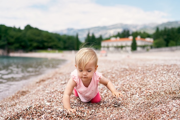 La bambina si inginocchia su una spiaggia di ciottoli vicino all'acqua