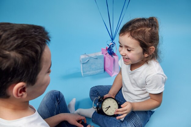 Bambina che ride con una sveglia in mano e seduto di fronte a un ragazzo sulla superficie blu