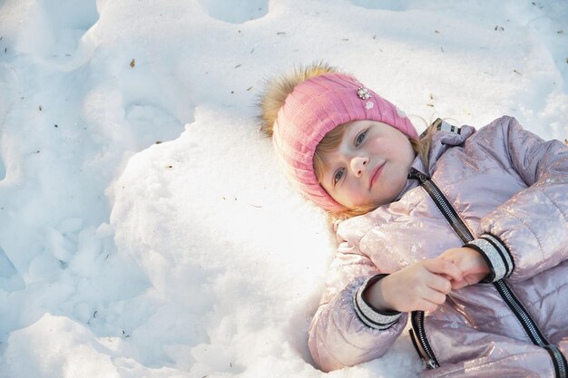 Little girl lays on the snow copy space top view