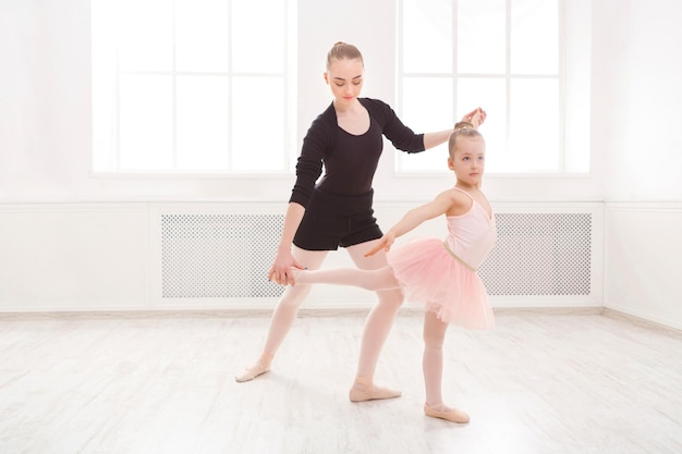 Little girl learning ballet with teacher copy space. Cute small ballerina training classical dance exercises with female coach.