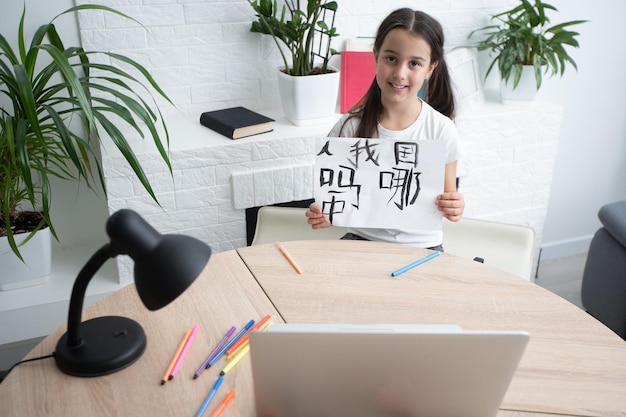 little girl learning chinese while using her laptop computer in the living room at home. family activity concept.