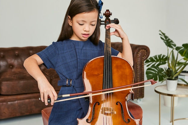 家でチェロを弾く方法を学ぶ少女