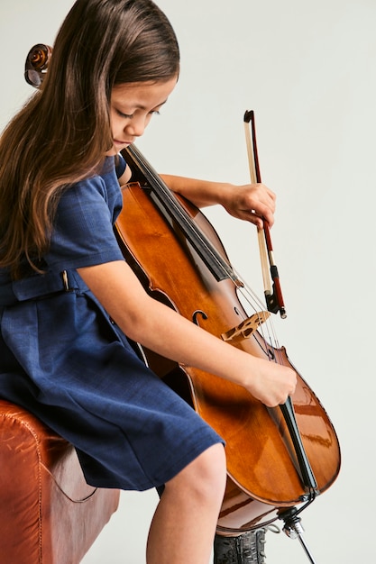 写真 家でチェロを弾く方法を学ぶ少女