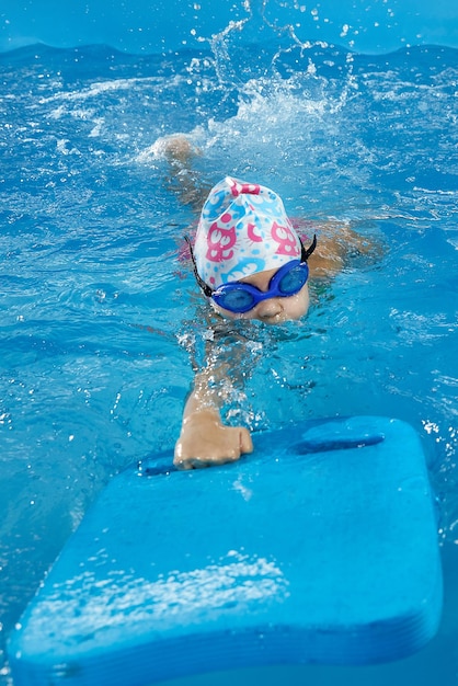 Маленькая девочка учится плавать в крытом бассейне с доской для бассейна