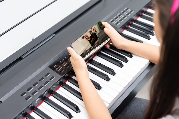 A little girl learns to play the piano from video lessons. Online distance learning during covid-19