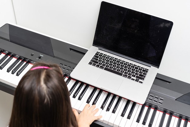 A little girl learns to play the piano from video lessons. Online distance learning during covid-19