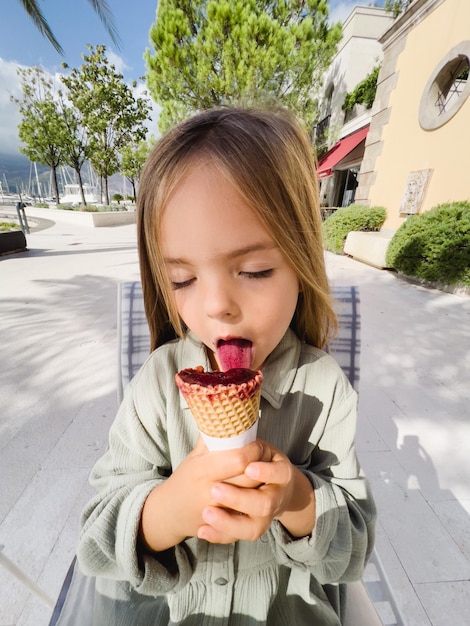 Photo little girl licks popsicles in a cone