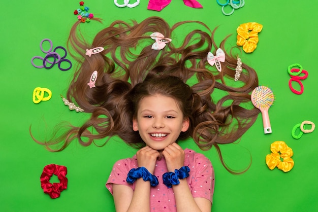 Una bambina giace tra le fasce per capelli e le forcine per capelli un  bambino con capelli sciolti e accessori per capelli giace su uno sfondo  verde isolato