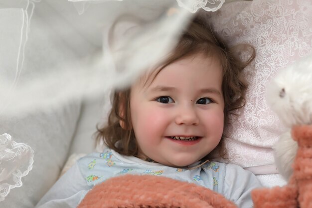 Little girl lies in bed on pillow and smiles