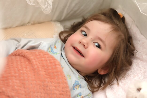 Little girl lies in bed on pillow and smiles