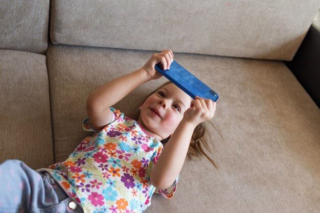 A little girl lies on the couch and looks at the phone