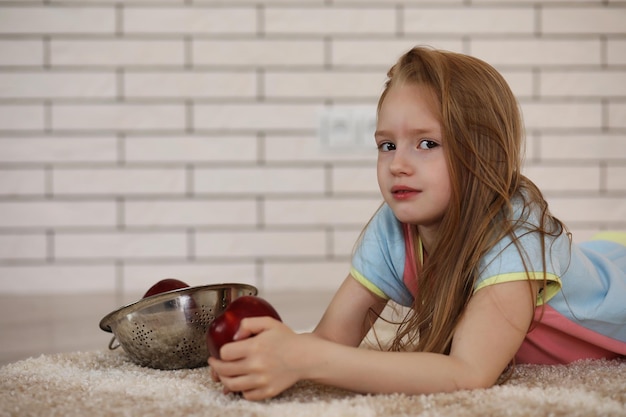 little girl lies on the floor and eats an apple