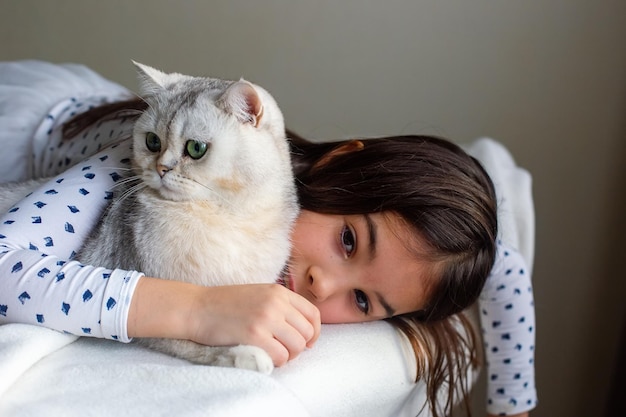 The little girl lies with a white cat on the bed