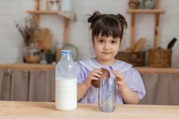 薄紫色のドレスを着た少女は牛乳を飲み、台所のテーブルでパンを食べます。テキスト、バナー用のスペース