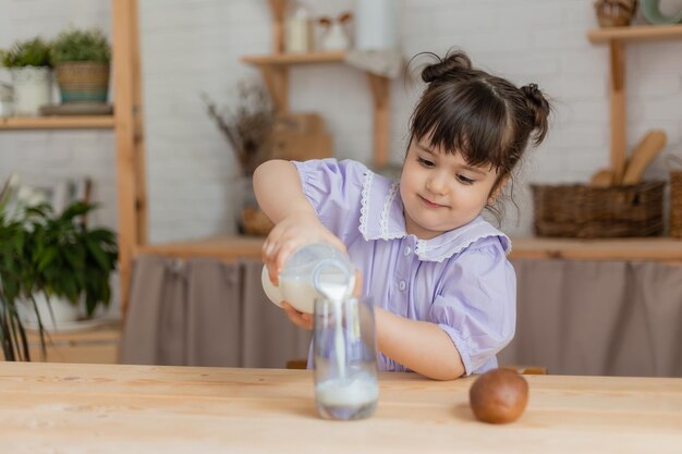 薄紫色のドレスを着た少女は牛乳を飲み、台所のテーブルでパンを食べます。テキスト、バナー用のスペース