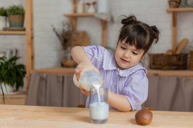 薄紫色のドレスを着た少女は牛乳を飲み、台所のテーブルでパンを食べます。テキスト、バナー用のスペース