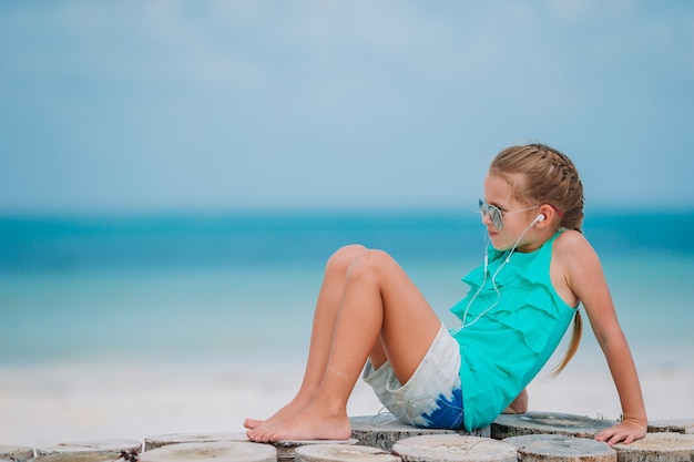 Little girl listening to music on headphones on caribbean beach