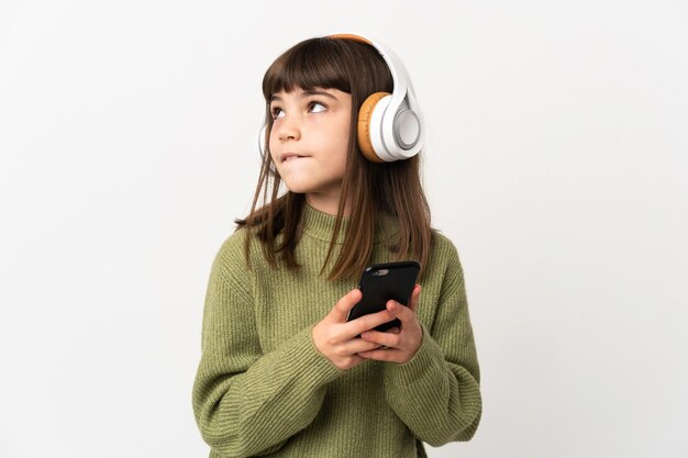 白い背景で隔離の携帯電話で音楽を聴いている少女携帯電話で音楽を聴いて考えている