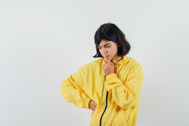 Little girl looking down while thinking in yellow hoodie and looking indecisive. front view.