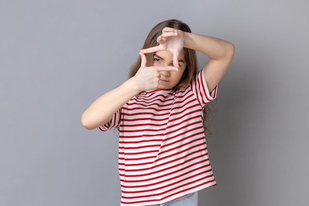 Little girl looking through fingers imagining frame to make good photos dreaming to be photographer