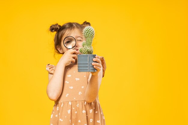 A little girl looks at a cactus under a magnifying glass