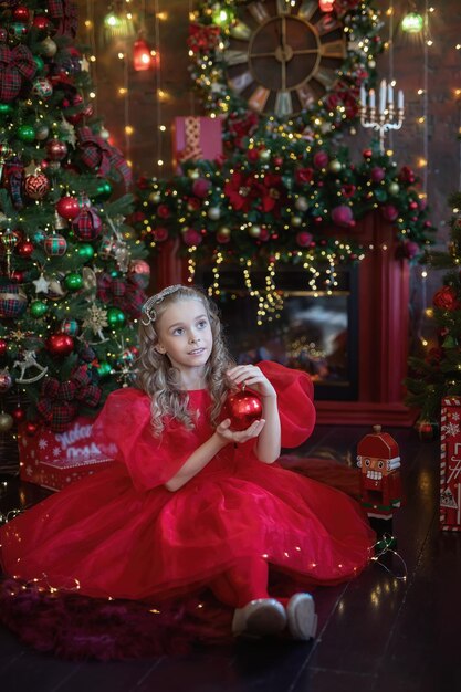 Little girl looks at Christmas decorations sitting under the Christmas tree