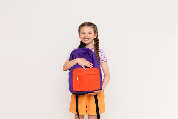 A little girl looks into a school backpack with books How to pack a backpack for school A beautiful child with pigtails and shorts on a white isolated background