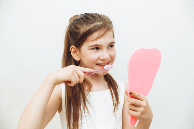 La bambina si guarda allo specchio e si lava i denti su uno sfondo bianco igiene e cura dei denti