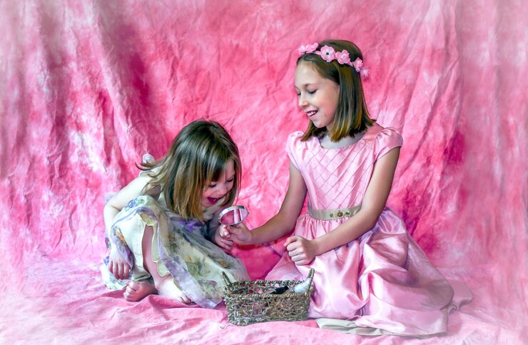Photo a little girl looks in a mirror held by her big sister and admires how pretty she looks