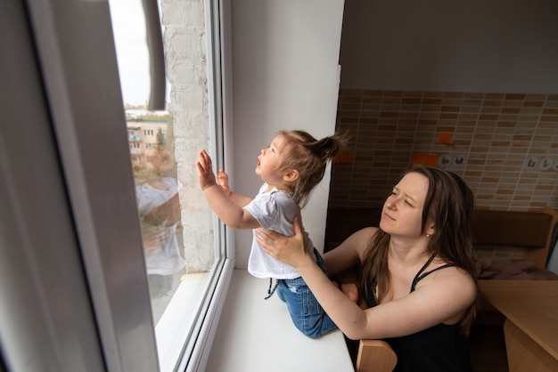 Little girl looks out the window and asks outside during quarantine caused by coronavirus.