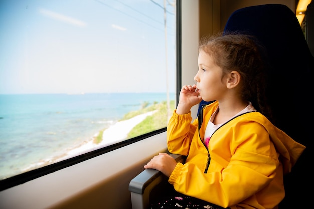 A little girl looks out the window of a train at the sea Reflection Vacation Summer Family vacation