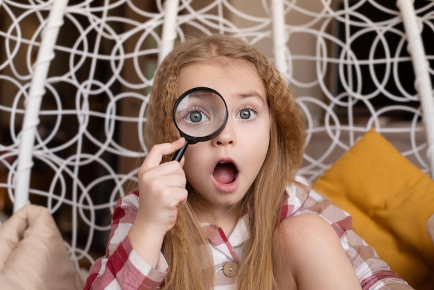 Photo a little girl looks through a magnifying glass, a child's surprise on her face